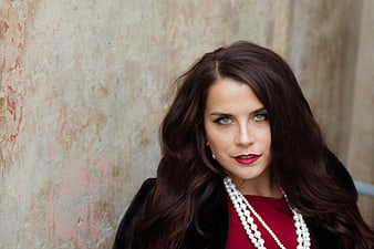 Stylish woman with red lipstick and pearls against textured wall