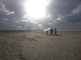 Family Flying Kites on Sandy Beach Under Dramatic Sunbeams