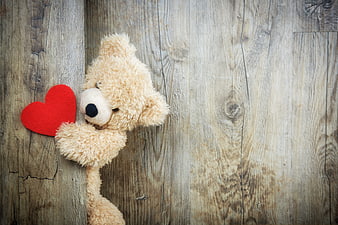 Cute teddy bear holding red heart on rustic wood background