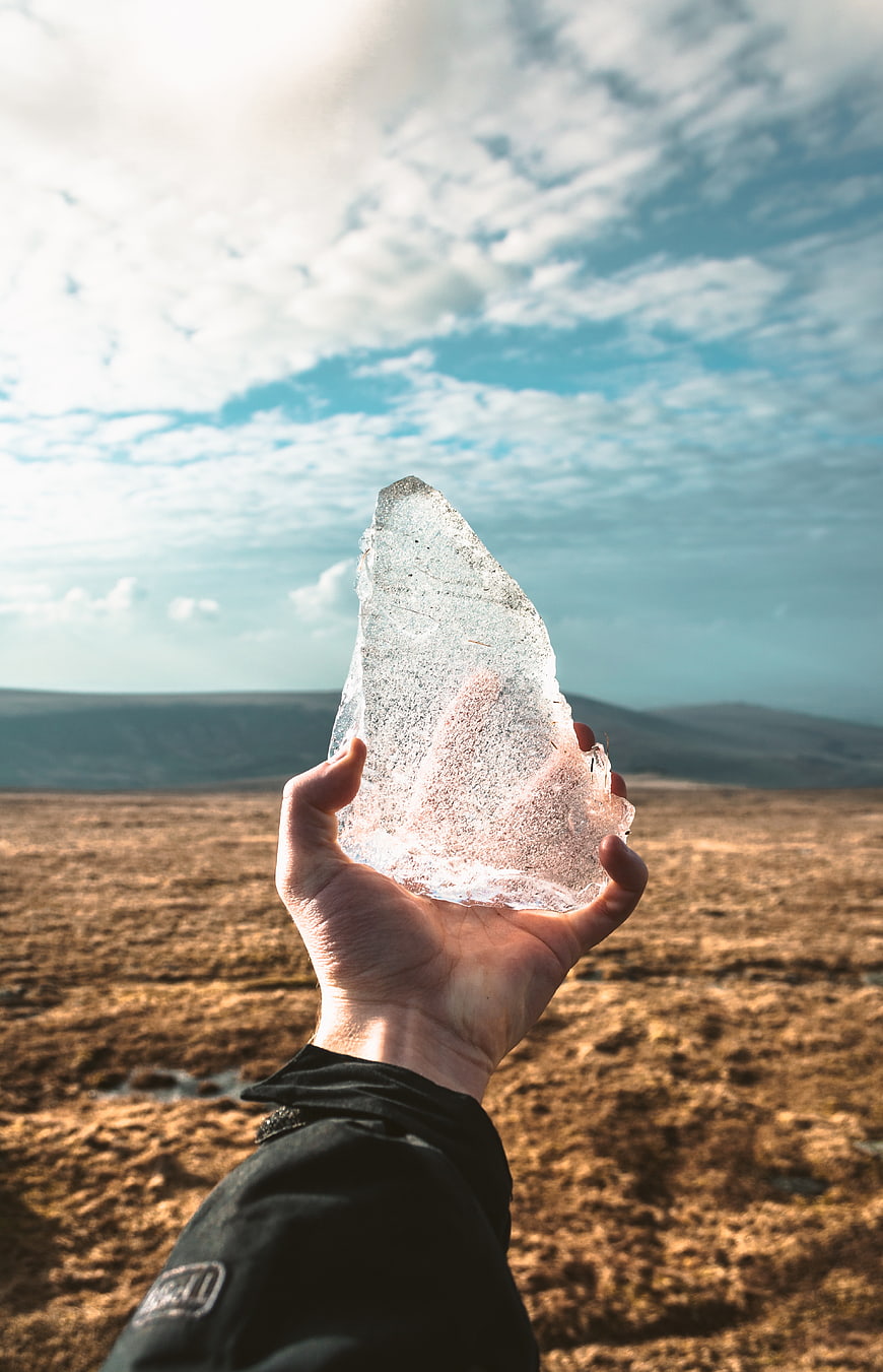 Hand holding clear ice crystal against mountain landscape