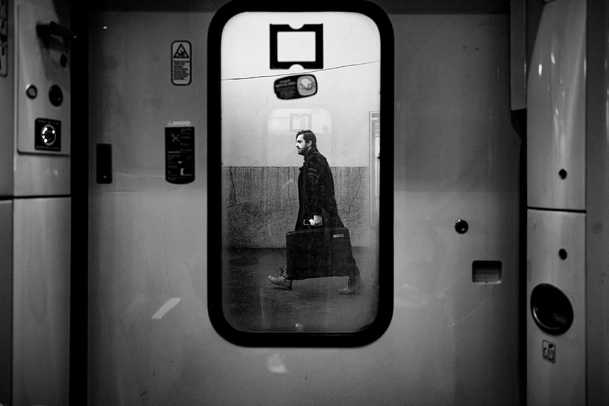 Man with suitcase walking past train window in black and white