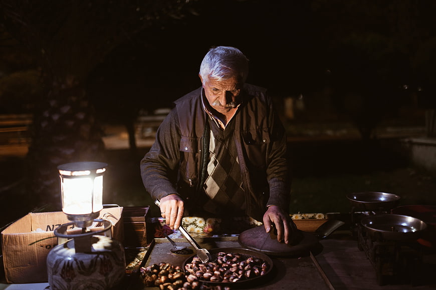 Elderly street vendor roasting chestnuts at night market