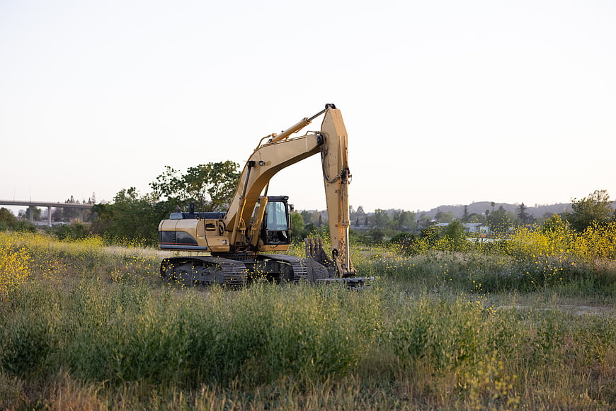 Yellow Excavator in Grassy Field with Wildflowers