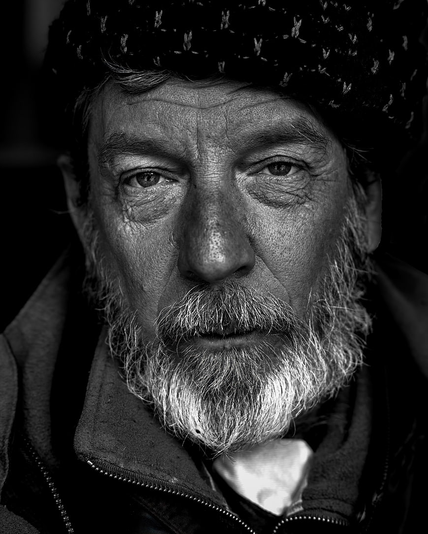 Black and white portrait of elderly homeless man with beard