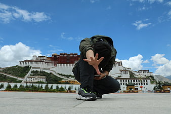 Young man crouching with smartphone in front of Potala Palace