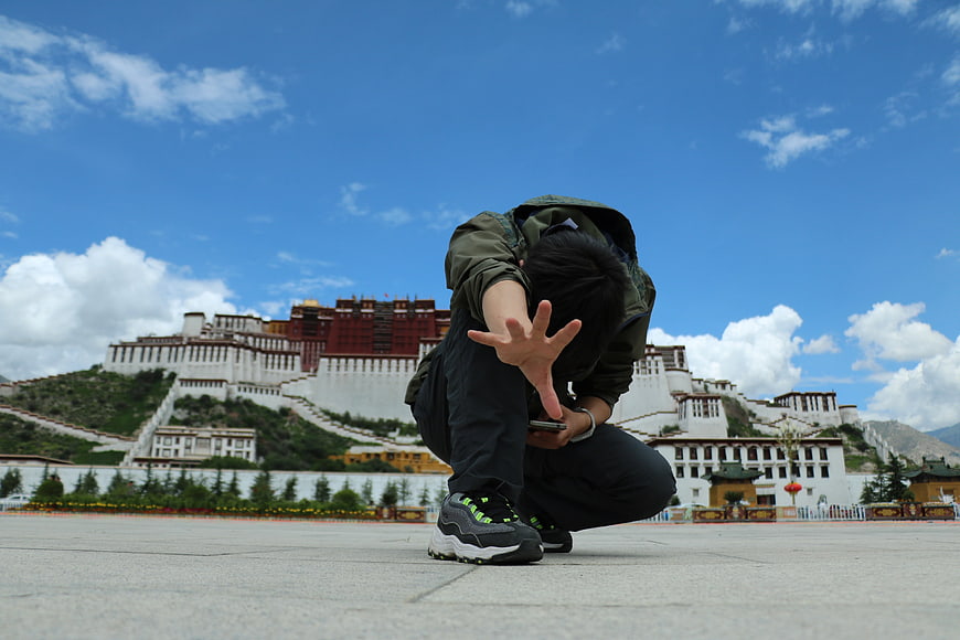 Young man crouching with smartphone in front of Potala Palace
