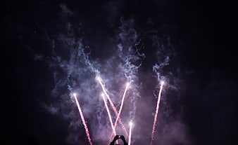 Silhouette of person filming fireworks display at night