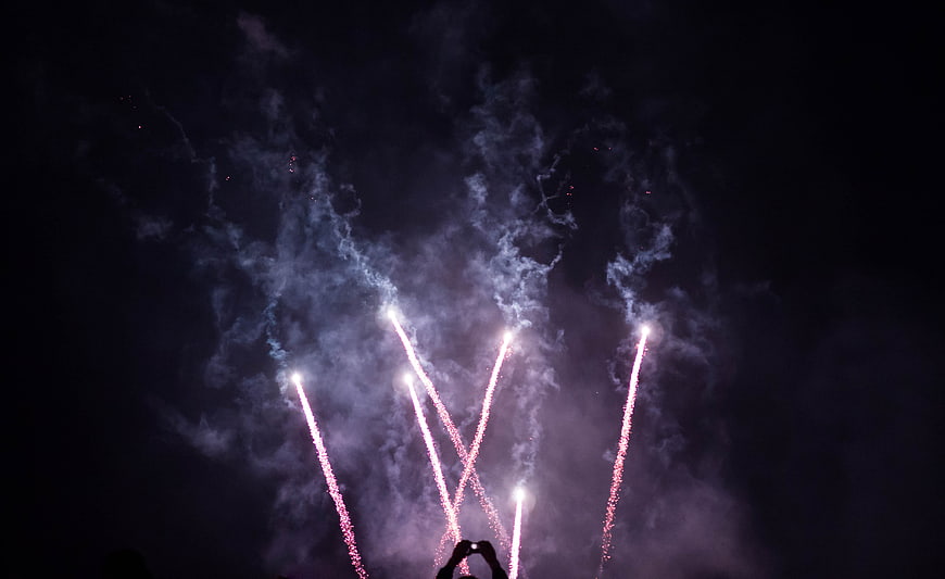 Silhouette of person filming fireworks display at night