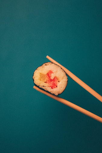Single piece of sushi held by chopsticks on teal background