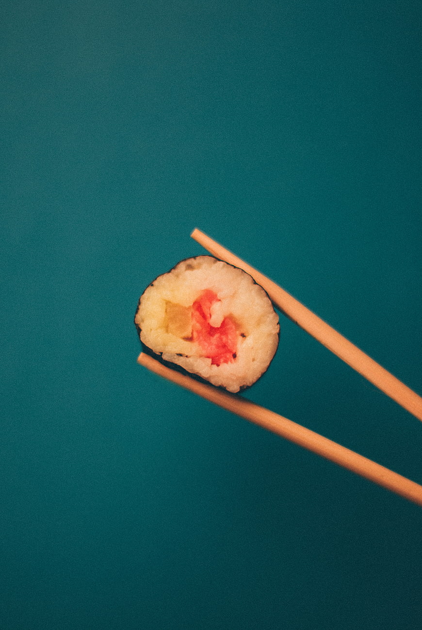 Single piece of sushi held by chopsticks on teal background