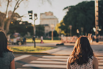 Two women standing at a city crosswalk in golden hour light