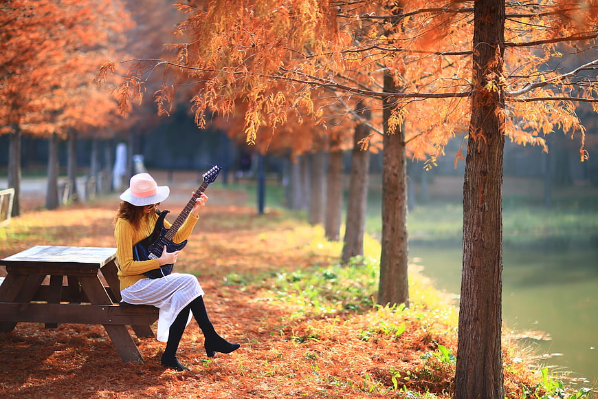 Woman Playing Electric Guitar On Picnic Table In Autumn Park