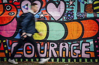 Man Walking Past Colorful Graffiti Wall with Courage Text