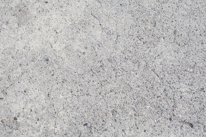 Close-up texture of weathered gray concrete wall with small cracks and pebbles