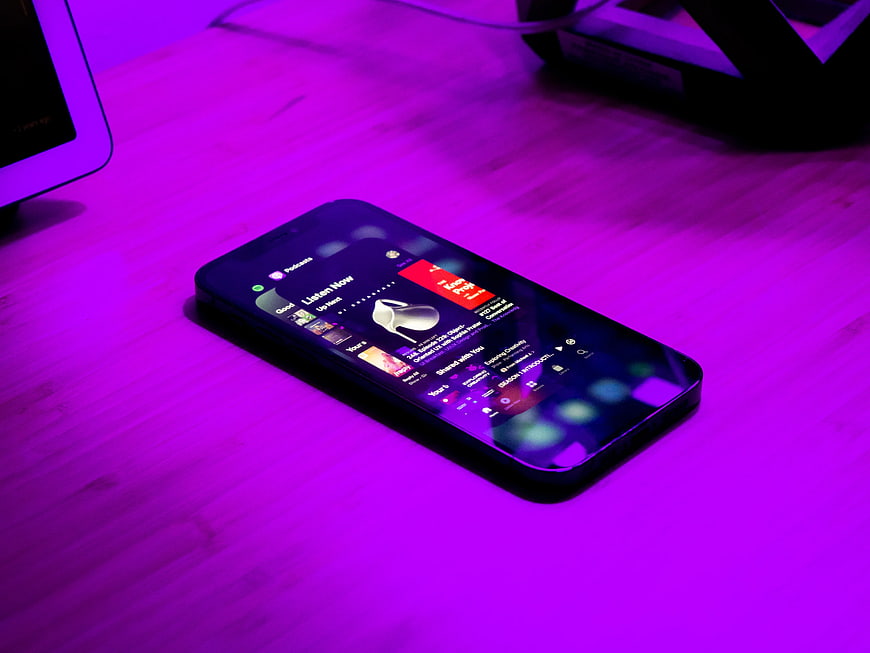 Smartphone displaying podcast app on purple lit desk