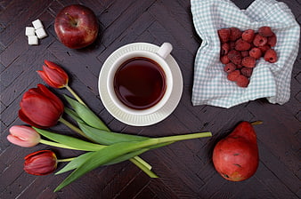 Flat lay of tea, tulips, apple, pear, and raspberries on dark wood