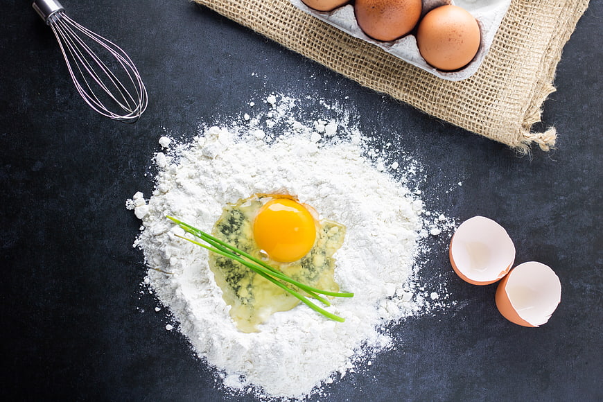 Baking ingredients with flour, egg, and chives on dark background