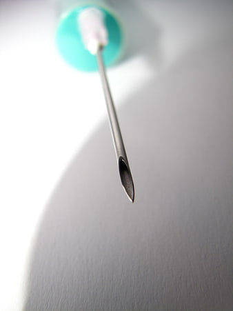 Close-up of a medical syringe needle tip on a white surface