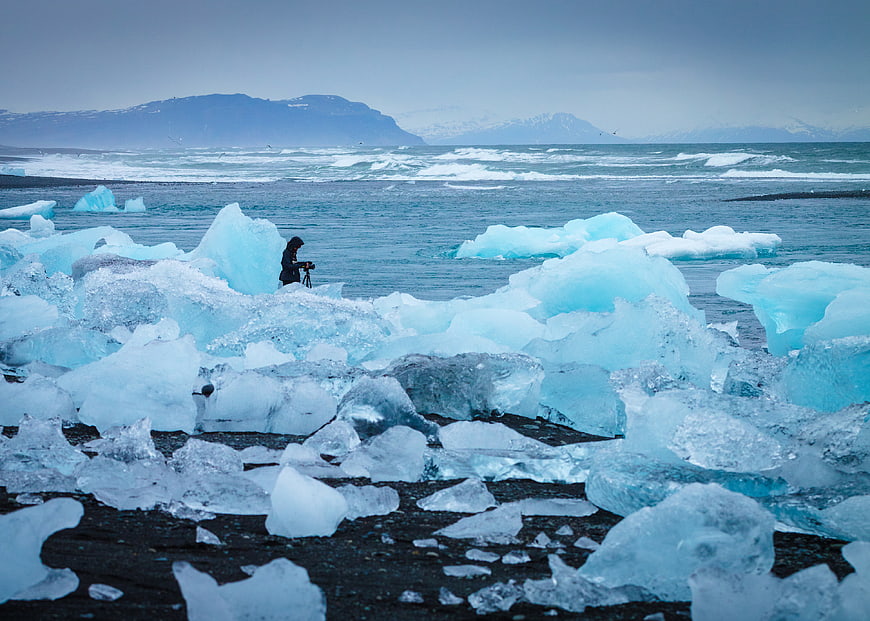 Photographer on Diamond Beach Iceland with Blue Icebergs