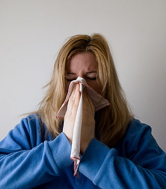 Blonde Woman Blowing Nose With Handkerchief Against White Background
