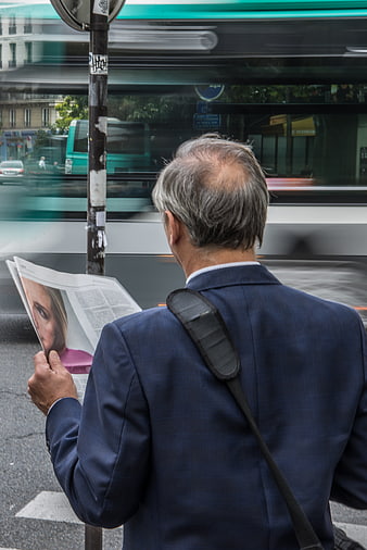 Senior businessman reading newspaper at busy bus stop
