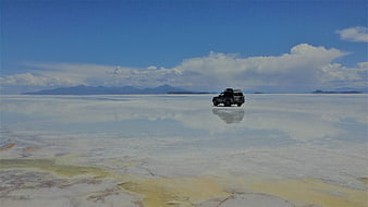 SUV driving on reflective salt flat landscape