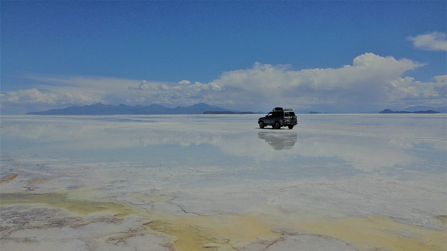 SUV driving on reflective salt flat landscape