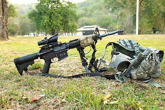 Military rifle and tactical backpack on grassy field