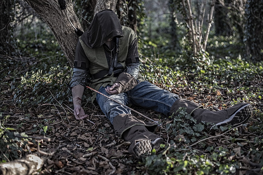 Hooded figure sitting in forest with self-harm scars
