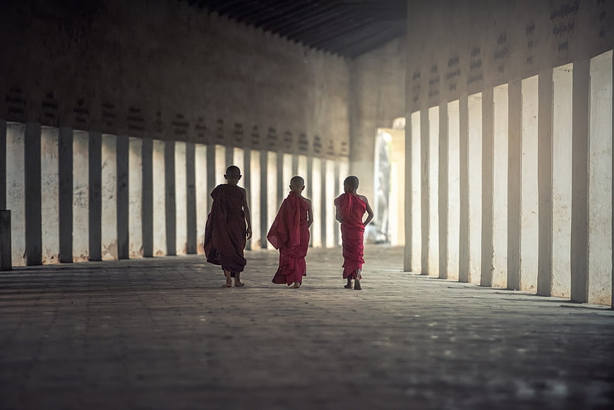 Three young Buddhist monks walking in a monastery hallway