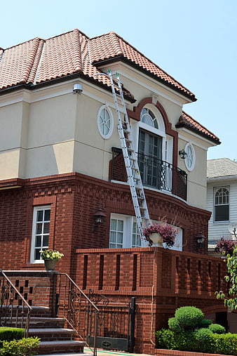 Aluminum ladder leaning against brick house for roof repair