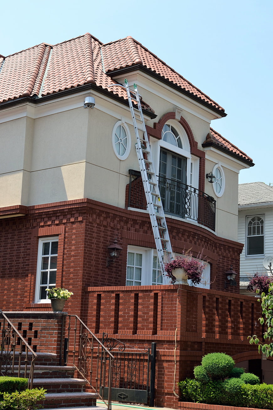 Aluminum ladder leaning against brick house for roof repair
