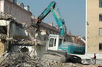 Excavator demolishing old building with construction worker