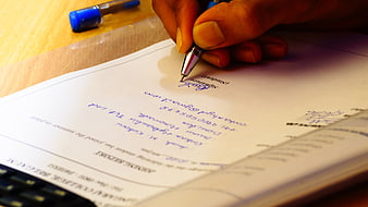 Hand Signing Document with Blue Pen on Desk