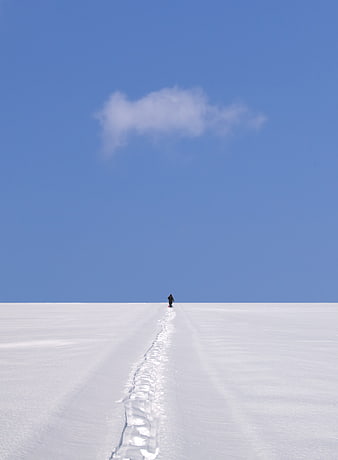 Lone figure walking on snowy path under blue sky