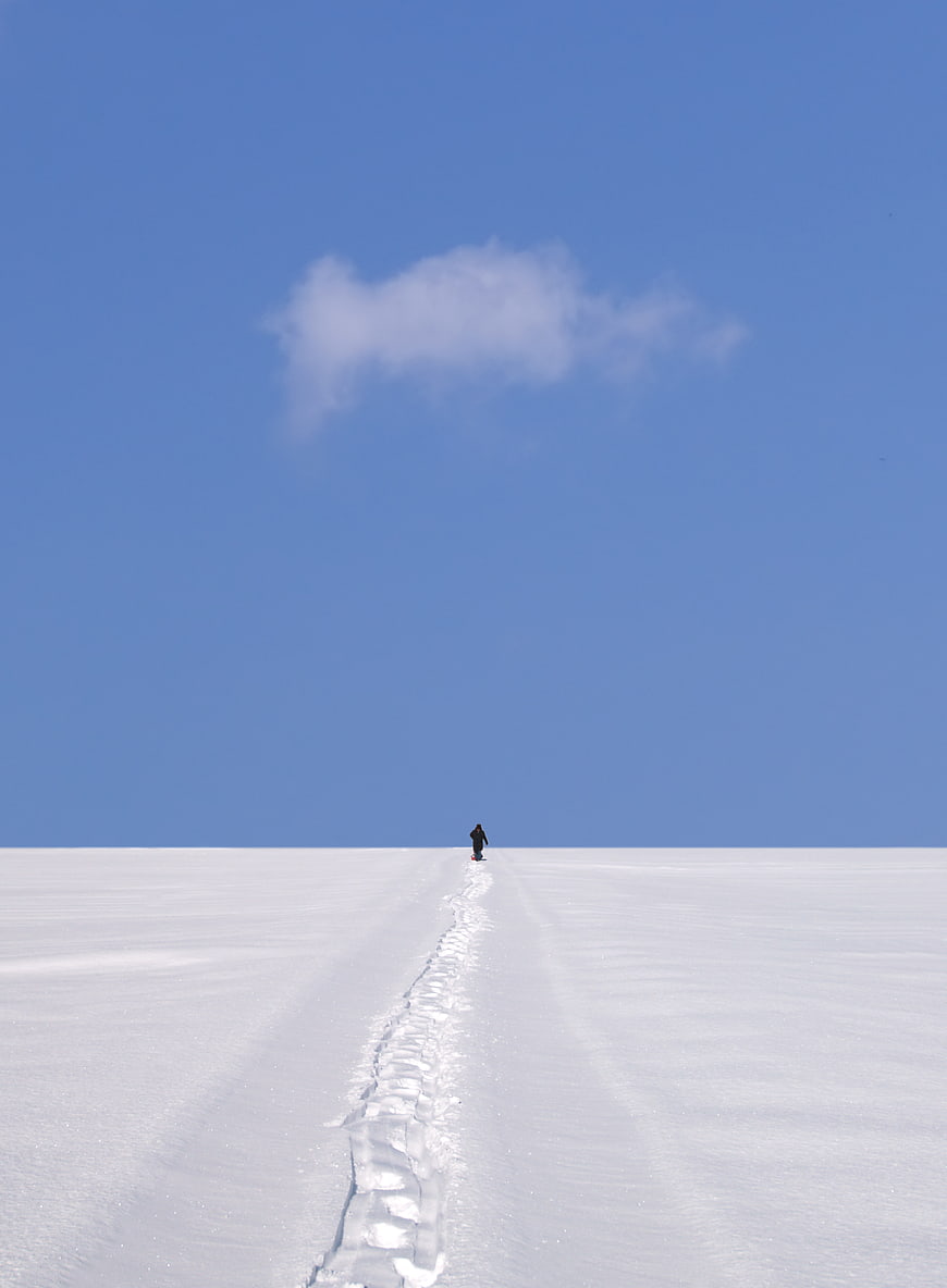 Lone figure walking on snowy path under blue sky