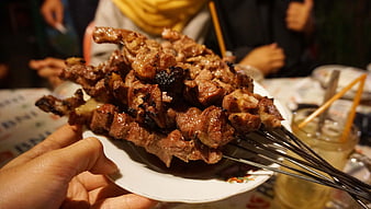 Hand holding plate of grilled meat skewers