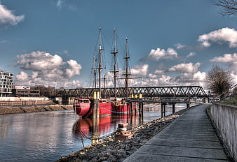 Red Tall Ship Moored in Harbor with Bridge