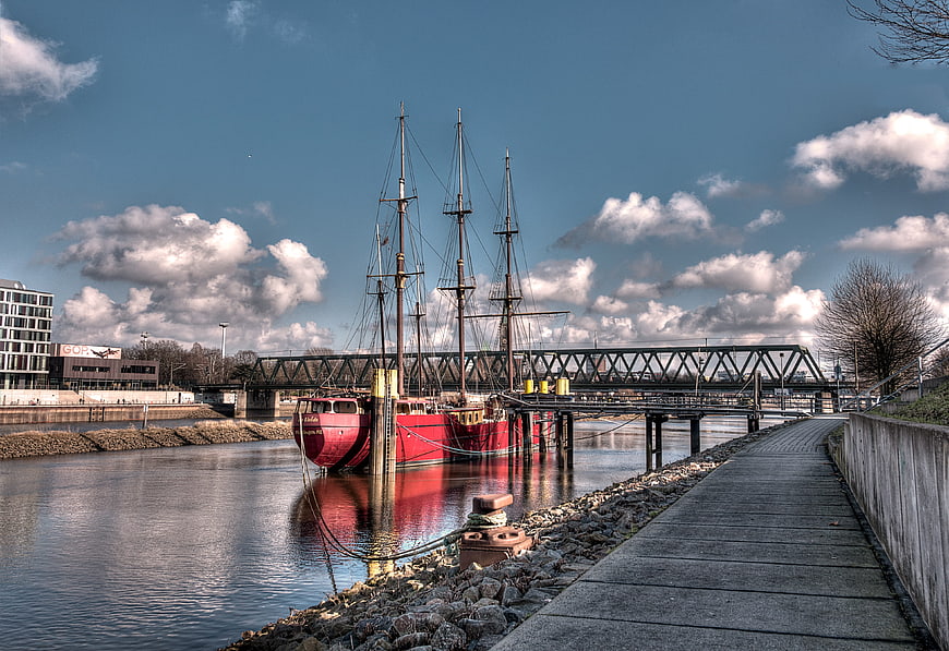Red Tall Ship Moored in Harbor with Bridge