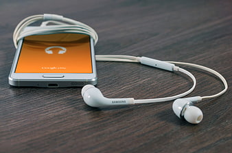 White Samsung smartphone with headphones on wooden table