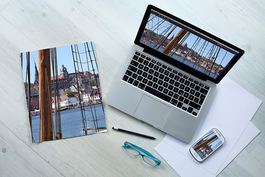 Laptop, smartphone, and print mockup of a harbor cityscape on a white wooden desk.