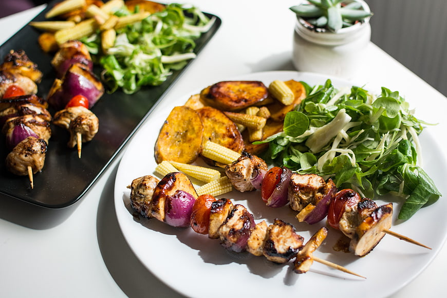 Grilled chicken skewers with plantains and salad on white plate