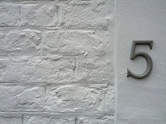 Metal number five on white textured brick wall