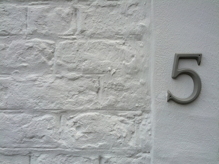 Metal number five on white textured brick wall