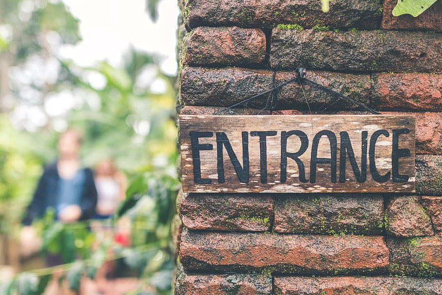 Rustic Wooden Entrance Sign on Mossy Brick Wall
