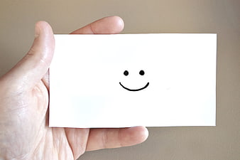 Hand holding white card with simple black smiley face drawing