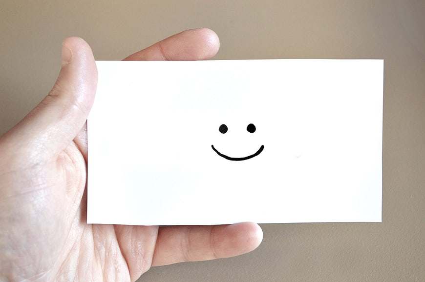 Hand holding white card with simple black smiley face drawing