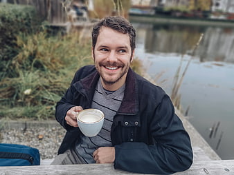 Smiling man holding coffee cup outdoors by a lake