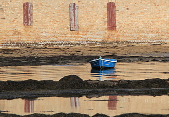 Blue boat moored in tidal waters near brick wall