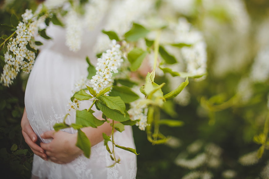 Pregnant Woman in White Dress Holding White Blossoms